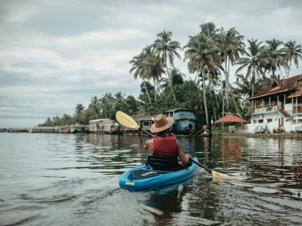 A kayaker paddling beside palms and waterfront buildings in Alleppey