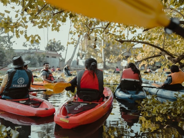 A group of kayakers in life jackets gathered on a leafy waterway